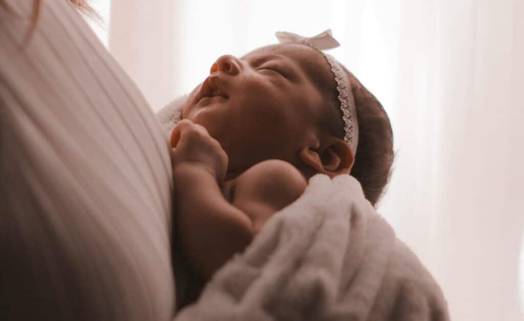 Serene image of a sleeping baby resting peacefully in a mother’s embrace. infant sleep schedule